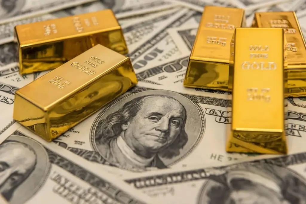 Five gold bars on top of spread out us 100 bills